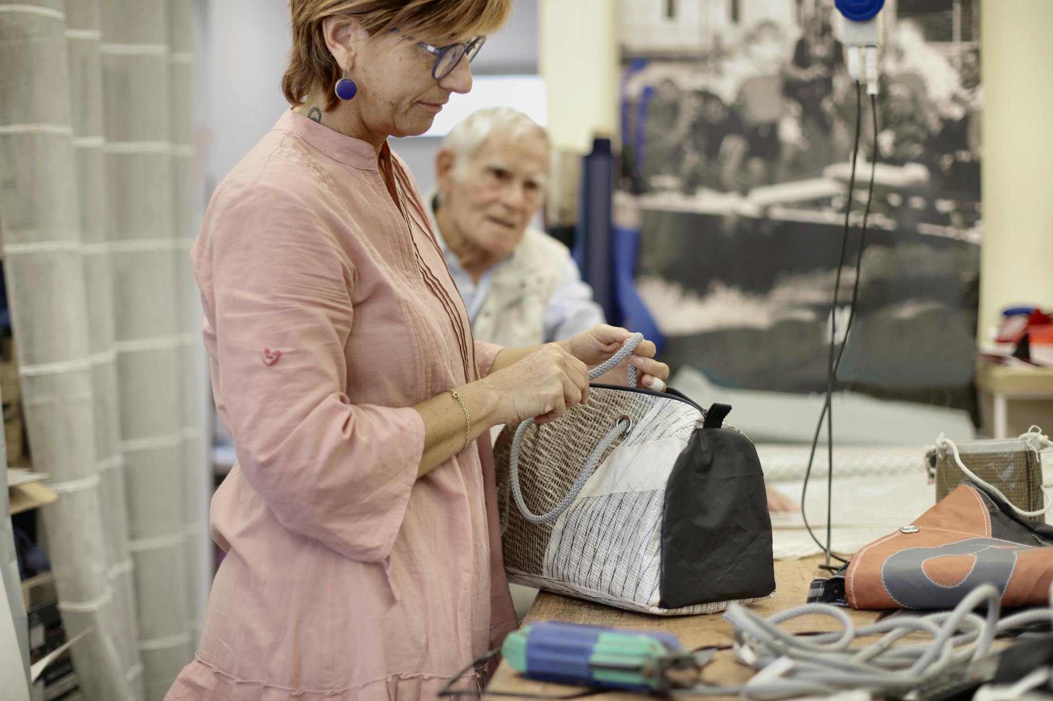 Side view of middle aged professional female master in casual wear checking details on fixed bag while working with customer in workplace